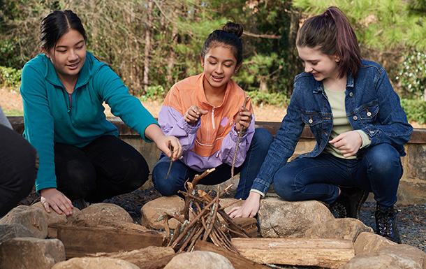 group of girl scouts around a campfire outside