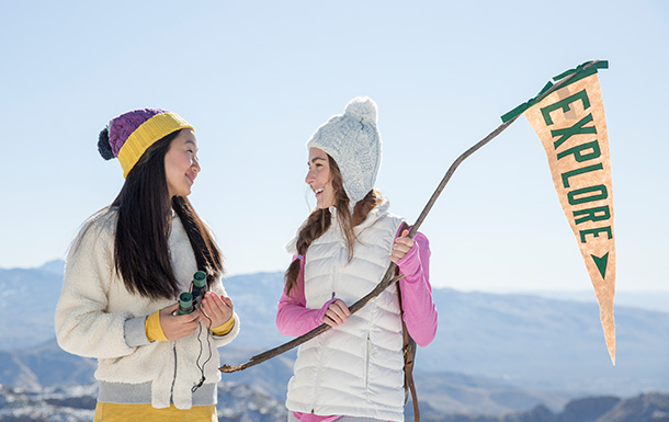 two high school girl scouts on mountain in winter clothes smiling holding flag that reads "explore"