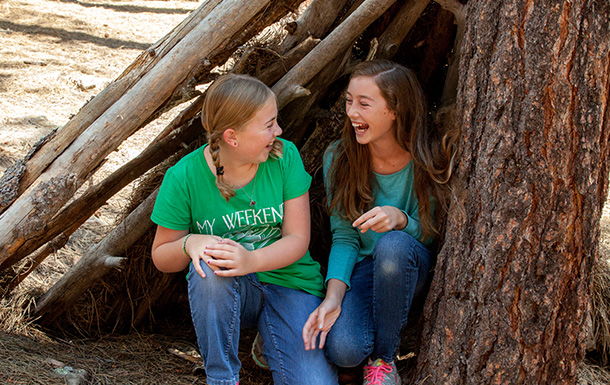 two girl scouts in a stick fort outside smiling and laughing
