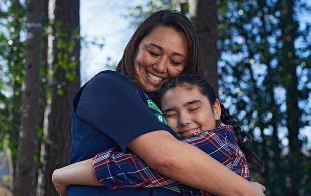 adult volunteer hugging girl scout outside in woods